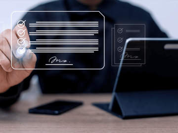 Ilustração digital de um homem de camisa escura sentado a uma mesa, tocando com o dedo em um documento virtual translúcido com itens marcados e uma assinatura, simbolizando a assinatura eletrônica de contratos. Ao fundo, um tablet apoiado sobre a mesa.